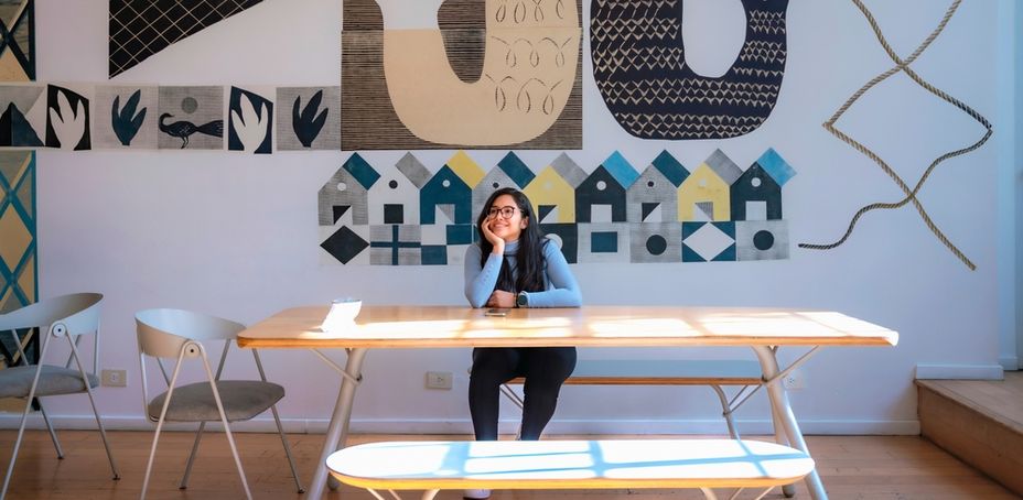 A woman sitting at a minimalist table in an office with geometric wall art.