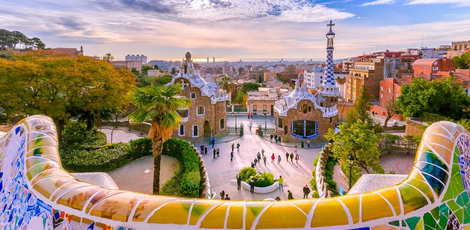 Sunset view of Park Güell's colorful mosaic structure with people enjoying the cityscape.